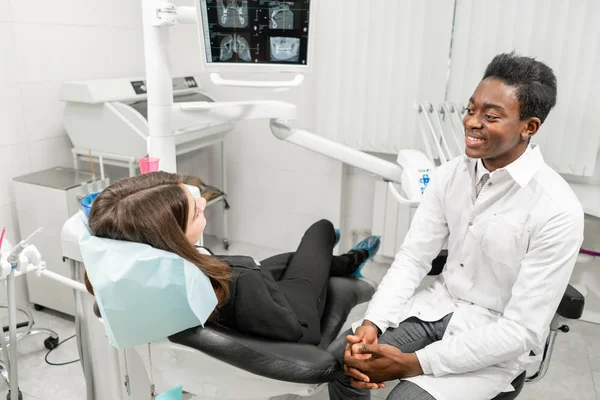 Joven dentista africano con un paciente. Mujer en la silla del dentista en la clínica dental. Medicina, salud, concepto estomatológico. dentista tratando a un paciente . — Foto de Stock