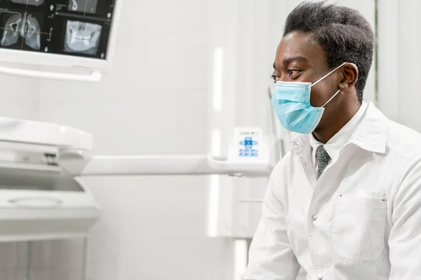 Un joven dentista africano muestra rayos X en el monitor. Medicina, salud, concepto estomatológico. dentista tratando a un paciente . — Foto de Stock