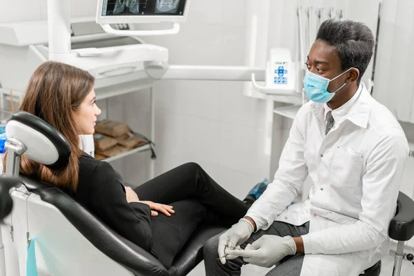 Mladý africký zubař s pacientem. Žena v zubařském křesle na zubařské klinice. Medicína, zdraví, stomatologie. zubař ošetřující pacienta. — Stock fotografie