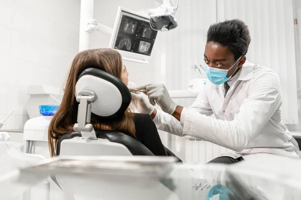Joven dentista africano con un paciente. Mujer en la silla del dentista en la clínica dental. Medicina, salud, concepto estomatológico. dentista tratando a un paciente . — Foto de Stock