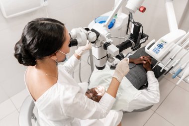 Genç kadın diş hekimi diş kliniğinde mikroskop kullanarak kök kanallar tedavi. Adam hasta ile açık ağız diş hekimi sandalyenin üstüne yalan. Tıp, diş hekimliği ve sağlık kavramı. Diş ekipman