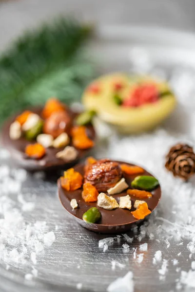 Christmas theme. Handmade chocolates candy. Mini chocolate dessert covered with nuts and dried fruits. Garland lamps bokeh on background. Copy space