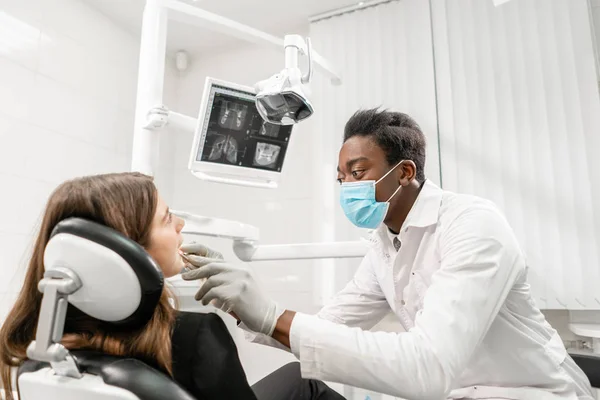 El doctor trata los dientes. Joven dentista africano con un paciente. Mujer en la silla del dentista en la clínica dental. Medicina, salud, concepto estomatológico. dentista tratando a un paciente . — Foto de Stock