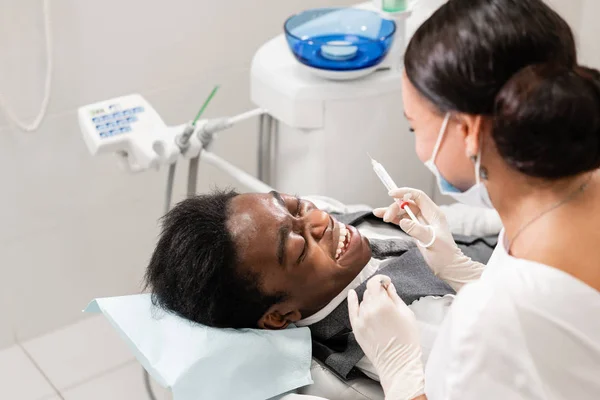 Jovem dentista tratando canais radiculares na clínica odontológica. Jovem afro-americano masculino com dentes ruins deitado na cadeira de dentista com boca aberta . — Fotografia de Stock
