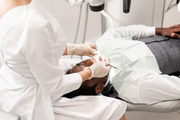 Mladá žena zubař léčení kořenových kanálků pomocí mikroskopu v zubní klinice. Muž pacient ležící na zubní křeslo s otevřenými ústy. Lékařství, zubní lékařství a zdravotnictví koncepce. Stomatologické zařízení — Stock fotografie