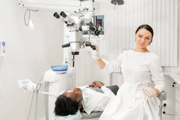 Portriat mladá žena zubař s mikroskopem. Pacientka leží na židli zubaře s otevřenou pusou. Koncepce medicíny, stomatologie a zdravotní péče. — Stock fotografie