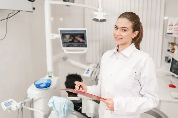 Encantadora doctora dentista hermosa. Joven paciente afroamericano en silla en la clínica dental. Medicina, salud, concepto estomatológico. dentista lleva a cabo la inspección y concluye. Mujer sonriendo — Foto de Stock