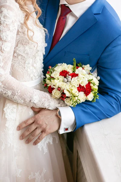 Bruid en bruidegom houden bruidsboeket close-up. rode en witte rozen, Freesia, brunia versierd. — Stockfoto