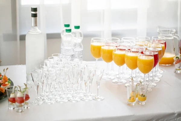 Table top full of glasses Glasses not alcoholic drinks, orange juice, water and berry juice. s with canapes and antipasti in the background.