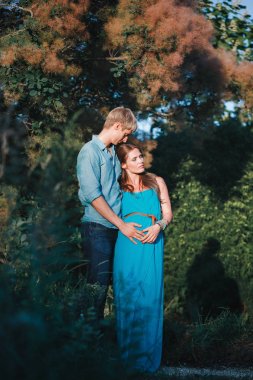 Genç güzel bir aile, müstakbel ebeveynler. Parkta hamile bir kadın. Üçüncü trimesterde sakin hamile kadın. Halka açık bahçede yürüyüş.