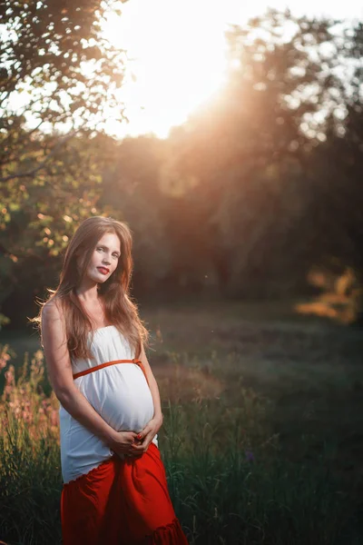 Junge schwangere Frau im Park im Freien. ruhige Schwangere im dritten Trimester. Wandern im öffentlichen Garten. Sonnenuntergang im Wald — Stockfoto