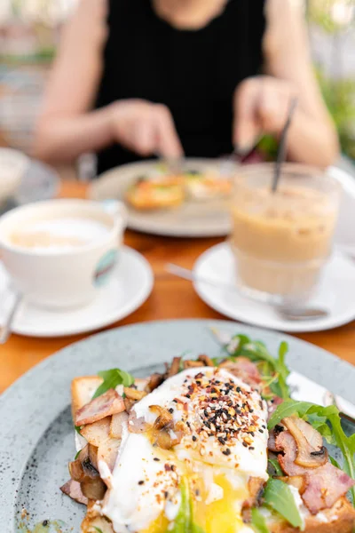 Petit déjeuner et café dans le café d'été. Sandwich sur brioche au bacon, champignons, roquette et oeuf poché — Photo