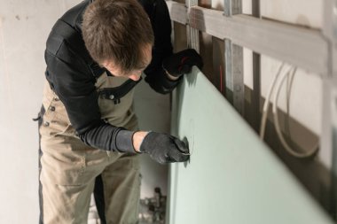 Builder çalışan bir adam elektrik kabloları için alçıpan bir işaret yapar. Yenileme sırasında bir evde metal alçıpan yapımı.