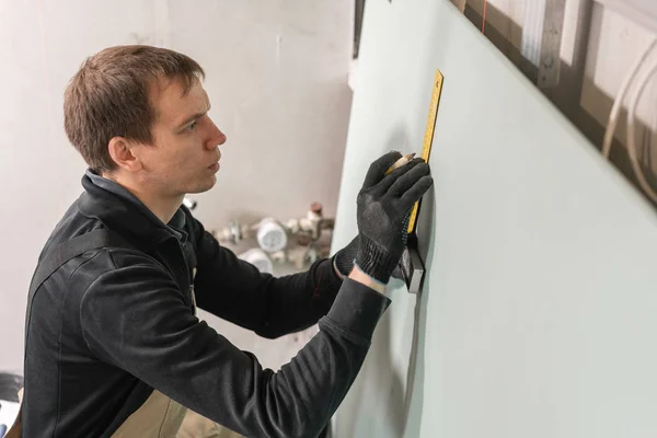 En man arbetar byggmästare gör en markering på för elektriska ledningar. Metall konstruktion i ett hus under renovering. — Stockfoto