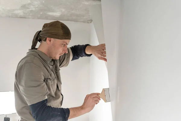 Young repairman smear on wall glue with a brush. Worker glueing wallpapers on concrete wall. Repair the apartment. Home renovation concept. White Wallpaper for paint — Stockfoto