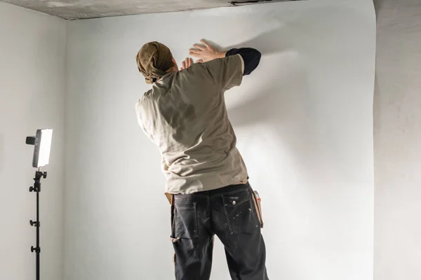 Worker applies a sheet of Wallpaper. Man glueing wallpapers on concrete wall. Repair the apartment. Home renovation concept. White Wallpaper for paint. step by step — 스톡 사진