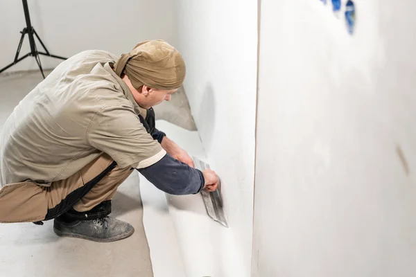 Worker applies a sheet of Wallpaper. Man glueing wallpapers on concrete wall. Repair the apartment. Home renovation concept. White Wallpaper for paint. step by step — Stockfoto