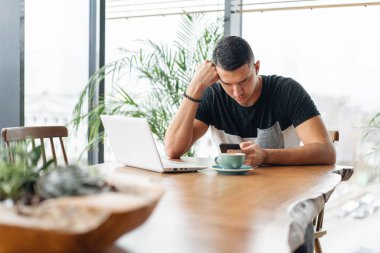 Freelancer iş modern coworking netbook üzerinde. Genç adam bir fincandan kahve içme. Programcı uzak iş. Başarılı insanlar, işadamı rahat kafede. Yüksek büyük pencereler