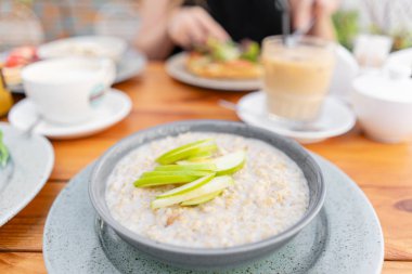 Yaz kafede kahvaltı ve kahve. Elma, bal, fındık ve tarçın ile taze yulaf püresi sağlıklı kahvaltı için yakın