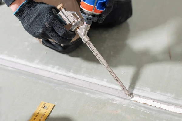 Arbetstagaren använder en polyuretanskum för limning gips på nittio grader. Handen håller polyuretan Expanderande skum lim pistol applikator — Stockfoto