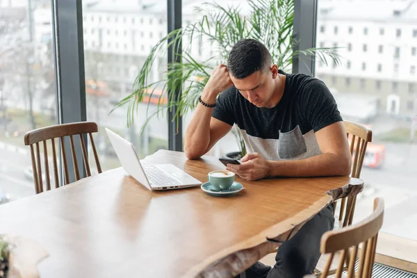 Freelancer arbete på netbook i moderna coworking. Ung man dricka kaffe ur en kopp. Programmerare på remote jobb. Framgångsrika människor, affärsman i bekväm café. Höga stora fönster — Stockfoto