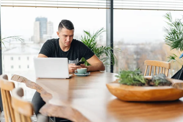 Freelancer arbete på netbook i moderna coworking. Ung man dricka kaffe ur en kopp. Programmerare på remote jobb. Framgångsrika människor, affärsman i bekväm café. Höga stora fönster — Stockfoto