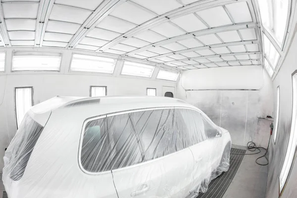 Garage painting car service. Vehicle is covered with protective paper. Repairing car body work after the accident by working sanding primer before painting.