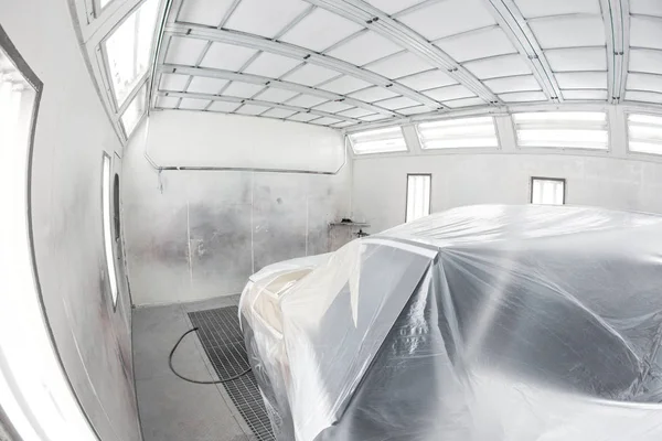 Garage painting car service. Vehicle is covered with protective paper. Repairing car body work after the accident by working sanding primer before painting.