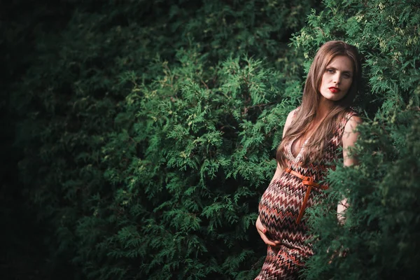 屋外の公園で若い妊娠中の女性。第3学期の穏やかな妊婦。公共の庭を歩く。森の中の木々 — ストック写真