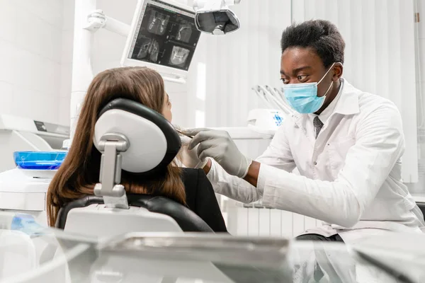 El doctor trata los dientes. Joven dentista africano con un paciente. Mujer en la silla del dentista en la clínica dental. Medicina, salud, concepto estomatológico. dentista tratando a un paciente . — Foto de Stock