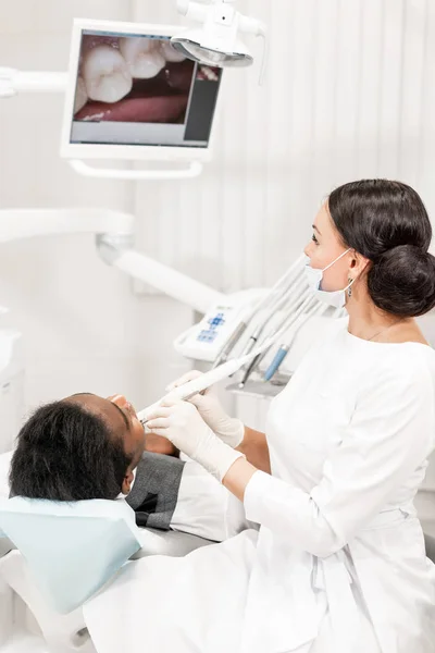 Kontrola s kamerou zubní makro a výsledek zobrazí na monitoru. Mladá žena zubař léčení kořenových kanálků v zubní klinice. Muž pacienta na zubní křeslo s otevřenými ústy. — Stock fotografie