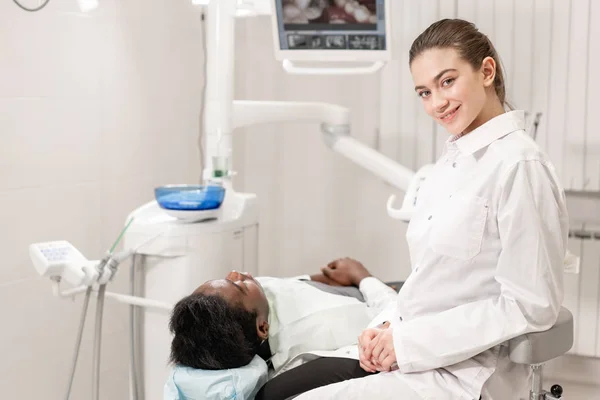 Rozkošný zubař doktor krásnou dívku. Mladý Američan Afričana pacient v křesle na zubní klinice. Lékařství, zdravotnictví, stomatologie koncept. zubní lékař provádí kontroly a uzavírá. Žena s úsměvem — Stock fotografie