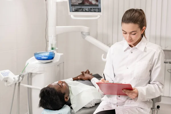 Rozkošný zubař doktor krásnou dívku. Mladý Američan Afričana pacient v křesle na zubní klinice. Lékařství, zdravotnictví, stomatologie koncept. zubní lékař provádí kontroly a uzavírá. Žena s úsměvem — Stock fotografie