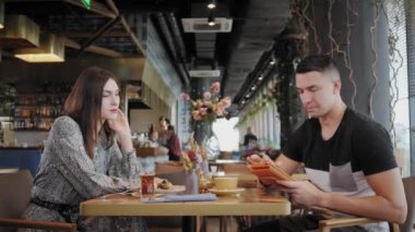 Genç adam tablet bilgisayarında yazıyor, sohbet ediyor, blog yazıyor. Başarılı insanlar, rahat bir kafede iş adamı. Yüksek Büyük Pencereler