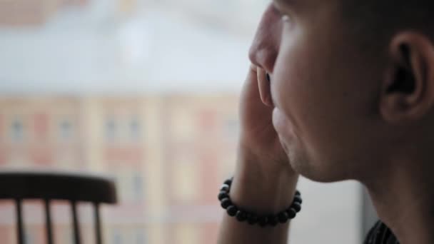 Le jeune homme parle par téléphone. Travail indépendant sur netbook en coworking moderne. Programmeur à distance. Des gens qui réussissent, un homme d'affaires dans un café confortable. Grandes fenêtres hautes — Video