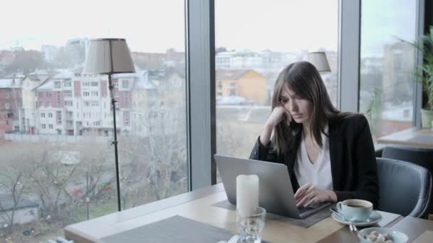 Indignado y con serias reacciones. Mujer joven sentada en la cafetería en la mesa de madera. En la mesa hay un portátil de aluminio gris. Chica blogging, navegar por Internet, chatear — Vídeos de Stock