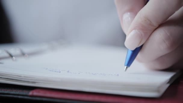 Close-up hand van een vrouw maken van notities in een notebook. Jonge zakenvrouw zittend in coffeeshop aan houten tafel. Op tafel is grijs aluminium laptop. Schema's en maakt belangrijke opmerkingen — Stockvideo