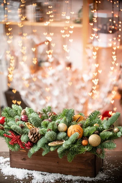 Χριστουγεννιάτικη διάθεση. Όμορφη εορταστική διαρρύθμιση του φρέσκου ερυθρελάτη σε ένα ρουστίκ ξύλινο κουτί. Οι καρδιές του Γκάρλαντ ανάβουν στο παρασκήνιο. Διακοσμημένο με φέτες πορτοκαλί, χρυσές μπάλες, κώνους — Φωτογραφία Αρχείου