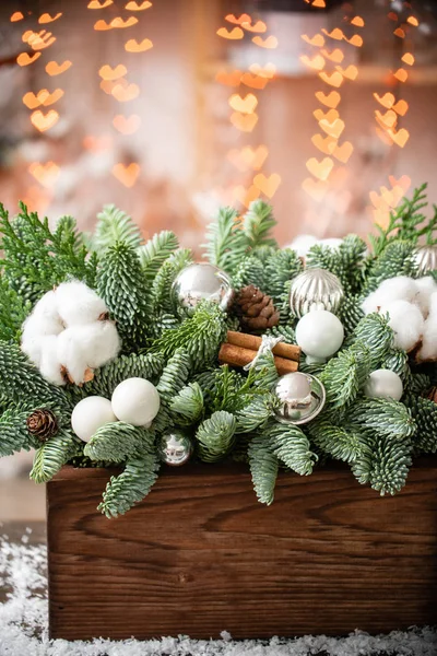 Χριστουγεννιάτικη διάθεση. Όμορφη εορταστική διαρρύθμιση του φρέσκου ερυθρελάτη σε ένα ρουστίκ ξύλινο κουτί. Οι καρδιές του Γκάρλαντ ανάβουν στο παρασκήνιο. Διακοσμημένο με καμπάνες, μπάλες ασήμι, λευκό βαμβάκι και κανέλα — Φωτογραφία Αρχείου