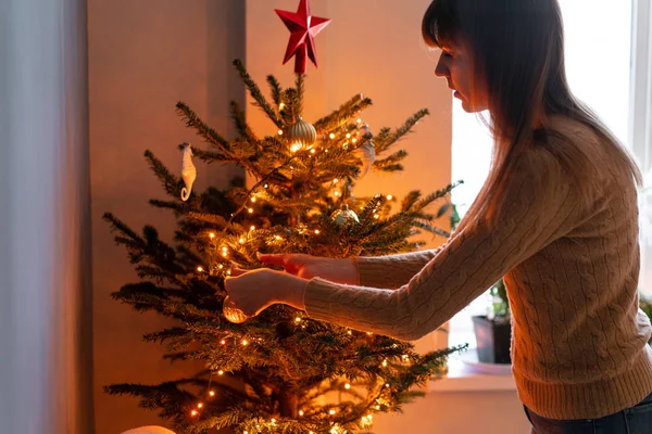 집에서 크리스마스 트리를 장식하는 행복한 젊은 여성. 집 인테리어의 겨울 휴가. 황금과 흰색 크리스마스 장난감, 조명 화환. 천연 덴마크 가문비 나무 — 스톡 사진