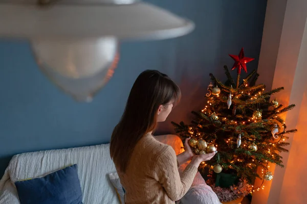 Gelukkig jonge vrouw versieren kerstboom thuis. Winter vakantie in een huis interieur. Gouden en witte kerst speelgoed, lichten slingers. Natuurlijk Deens sparrenhout — Stockfoto