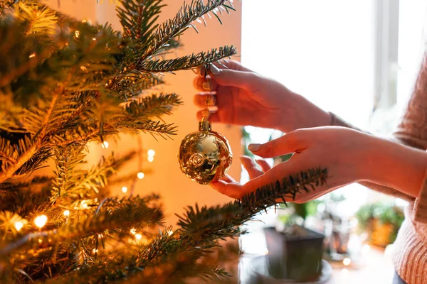 Férias de inverno em um interior de casa. Jovem feliz decorando árvore de Natal em casa. Brinquedos de Natal dourados e brancos, guirlandas de luzes. Abeto natural dinamarquês — Fotografia de Stock