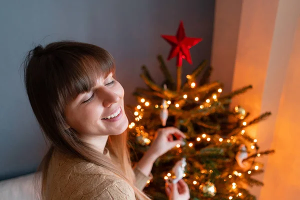 Gelukkig jonge vrouw versieren kerstboom thuis. Winter vakantie in een huis interieur. Gouden en witte kerst speelgoed, lichten slingers. Natuurlijk Deens sparrenhout — Stockfoto