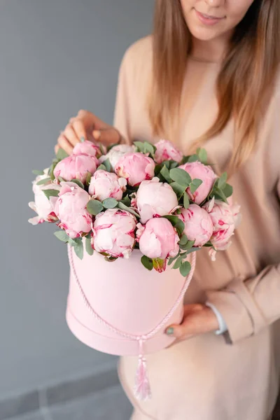 Peônias cor-de-rosa em caixa redonda rosa. Bela flor de peônia em mãos de mulheres de catálogo ou loja online. Conceito de loja floral. Entrega de flores — Fotografia de Stock