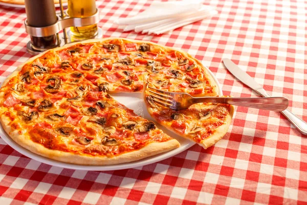 Närbild gaffel tar en bit. Pizza med skinka och svamp. Läcker varm mat skivad och serveras på vitt fat. Meny foto, italienska snabbmat. Royaltyfria Stockfoton