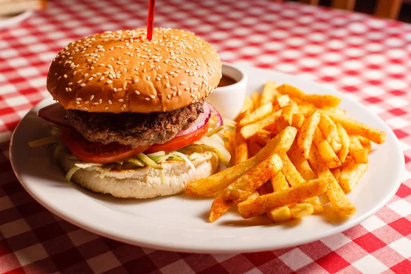 Sabrosa hamburguesa en el restaurante. Pan de sésamo, carne Patty, tomate, lechuga y pepinillo. Servido con papas fritas — Foto de Stock