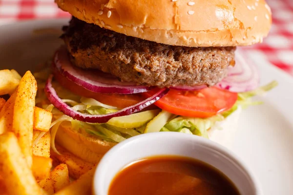 Cerrar Sabrosa hamburguesa en el restaurante. Pan de sésamo, carne Patty, tomate, lechuga y pepinillo. Servido con papas fritas — Foto de Stock