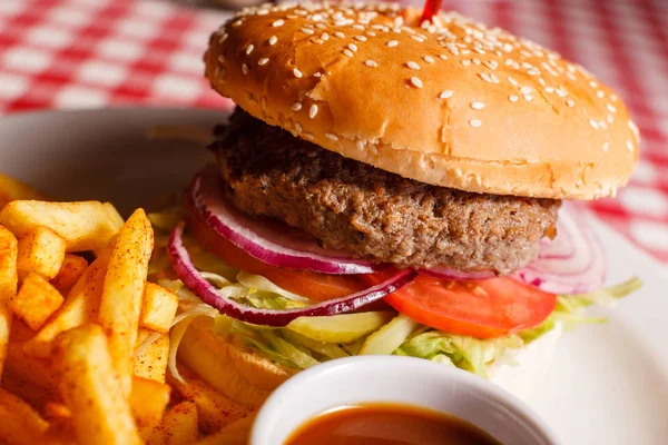 Sabrosa hamburguesa en el restaurante. Pan de sésamo, carne Patty, tomate, lechuga y pepinillo. Servido con papas fritas — Foto de Stock