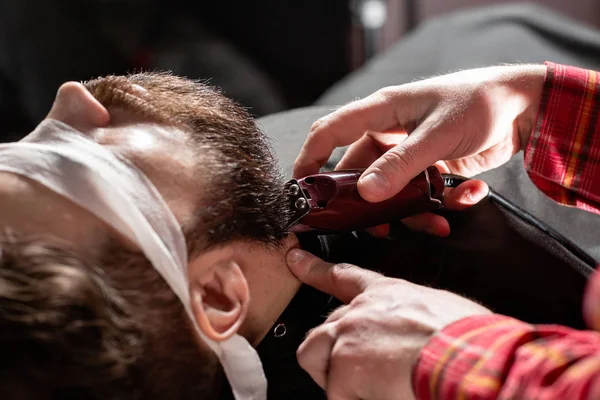 Sakal kesme, yüz bakımı. Berber dükkanında makas makinesi ile berber çalışır. Profesyonel düzeltici aracı berber dükkanı salonda genç adamın sakal ve saç keser. — Stok fotoğraf