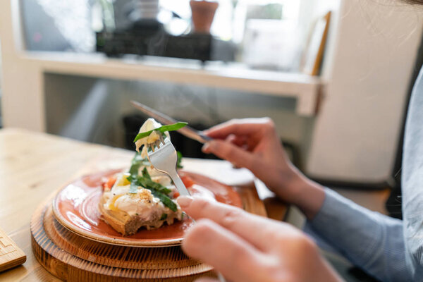Traditional Belgian waffle with salmon, lettuce leaves and poached egg. A young woman is having Breakfast in a cafe, hands with a fork and a knife close-up.
